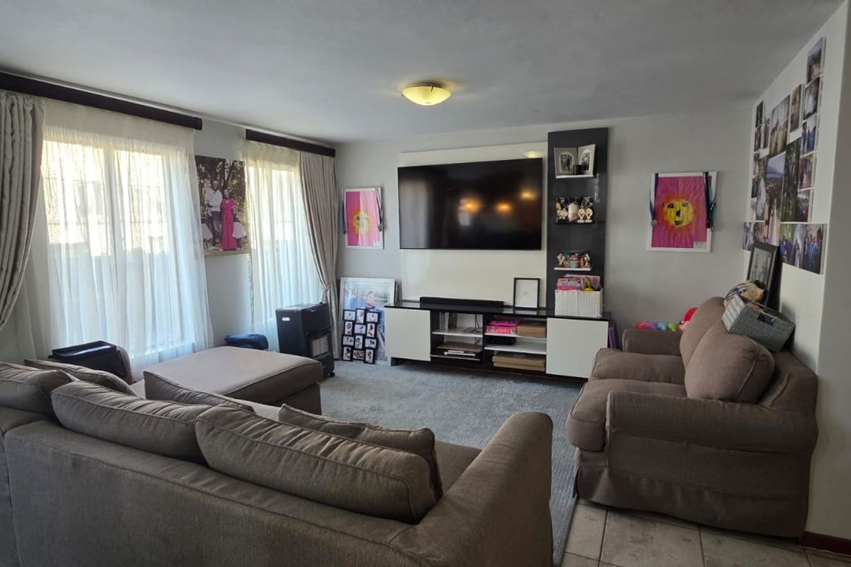 A comfortable living room featuring a built-in media unit, tiled flooring, and large windows with curtain tracks, providing a functional and well-lit space.