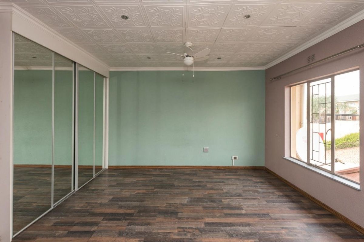 Spacious bedroom featuring decorative ceiling tiles, a ceiling fan, mirrored sliding wardrobes, and laminate flooring with security bars on the window.