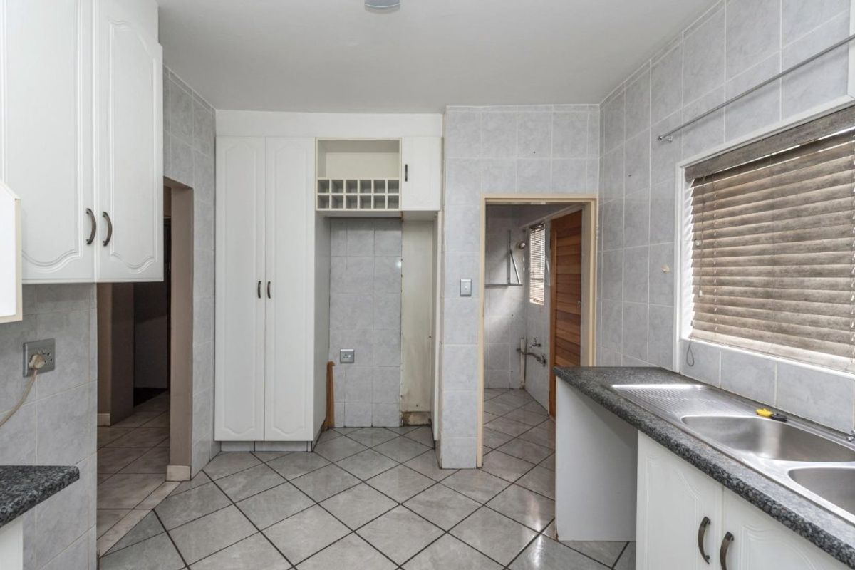 A functional kitchen featuring tiled walls and floors, granite countertops, a double bowl sink, and built-in cabinetry with an integrated wine rack.