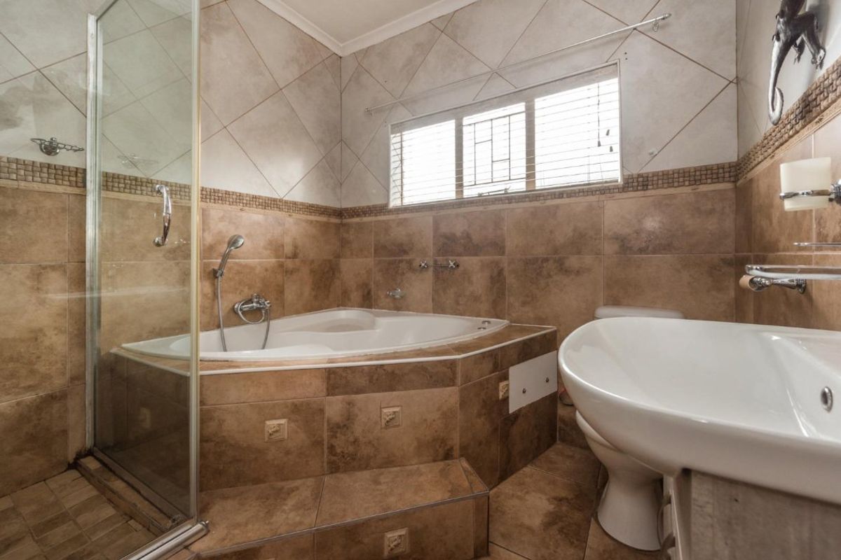 A dated bathroom featuring a corner bathtub, glass shower enclosure, pedestal basin, and tiled finishes throughout.