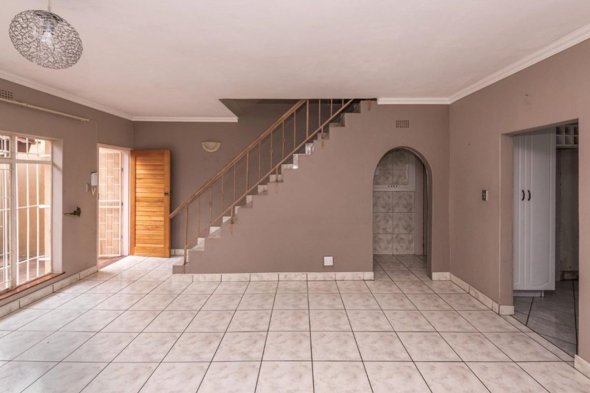 An open-plan living area featuring tiled flooring, a central staircase with metal balustrades, and an arched entryway leading to adjacent spaces.