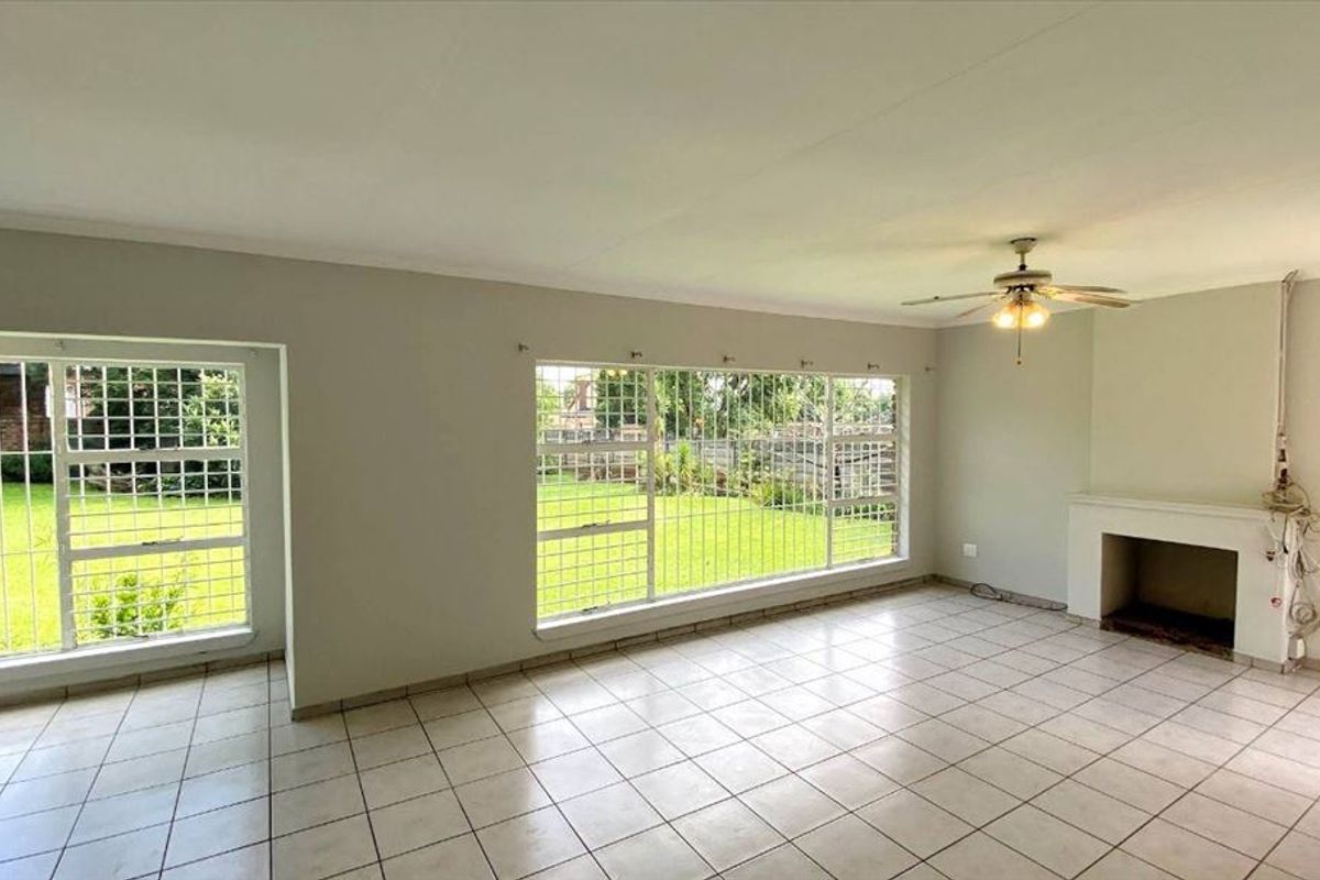 Spacious living room featuring tiled flooring, a ceiling fan, and a fireplace, with large windows providing views of the garden.