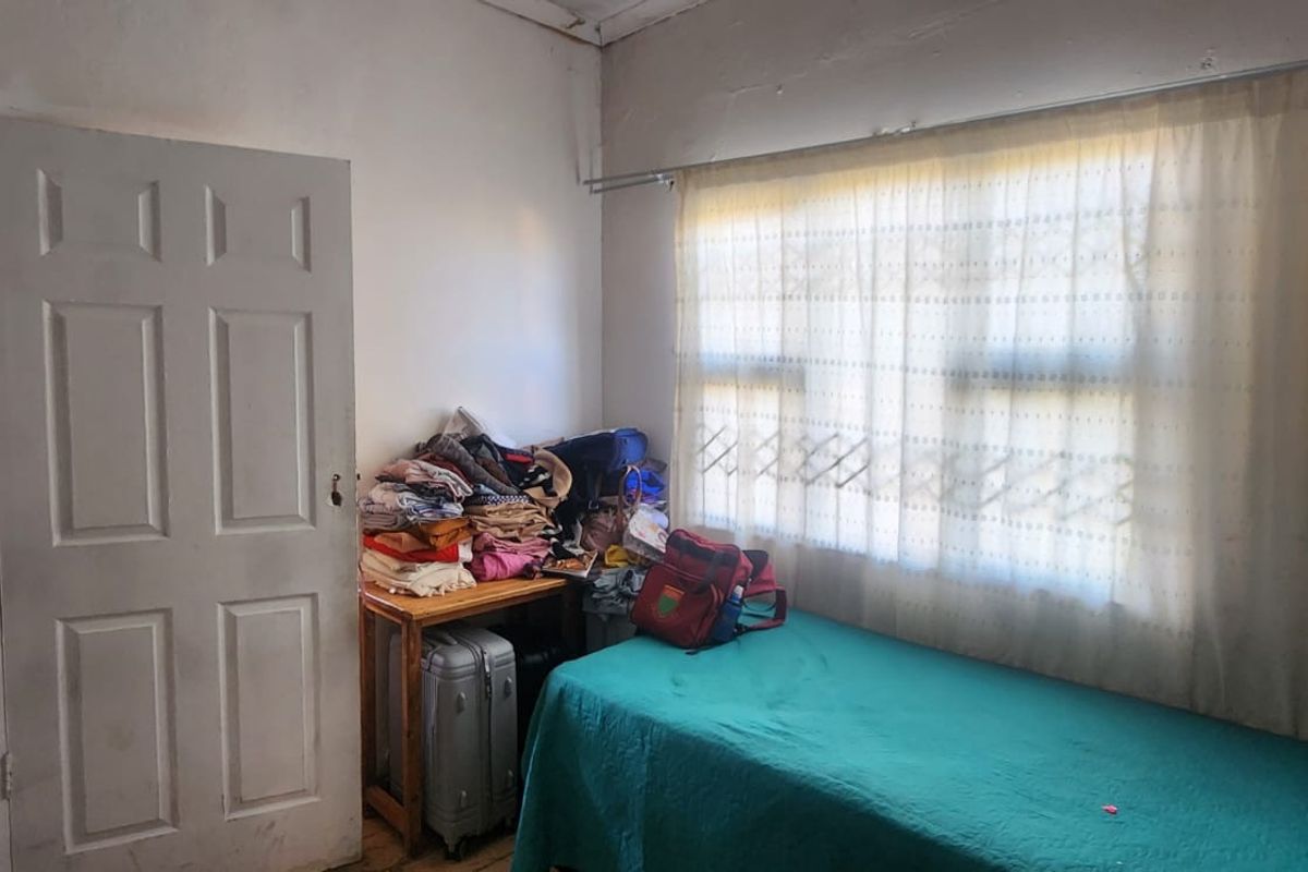A bedroom featuring a window with a curtain rail and visible wall surface deterioration requiring maintenance and cosmetic updates.