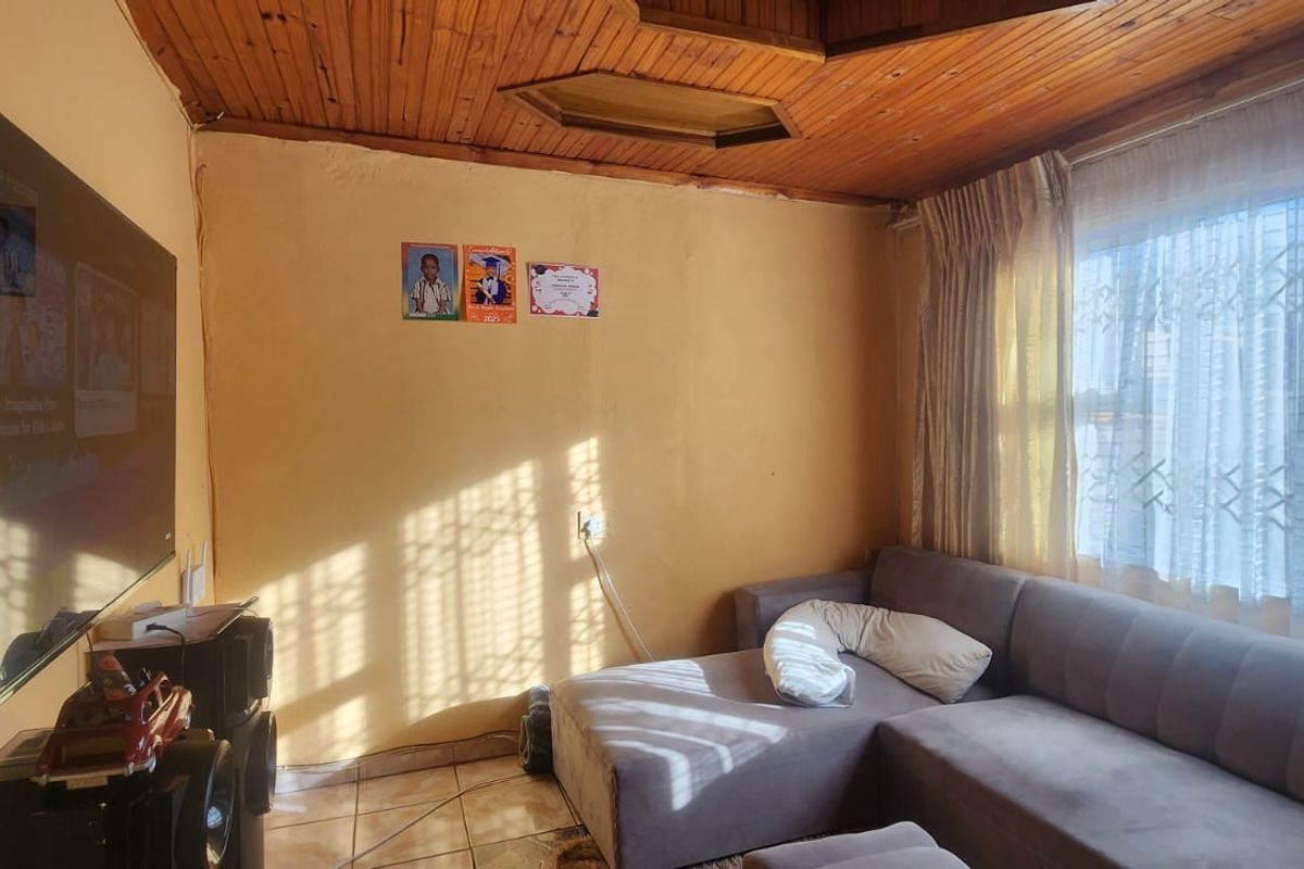 Living room featuring a timber tongue and groove ceiling, tiled flooring, and a window fitted with a security gate.