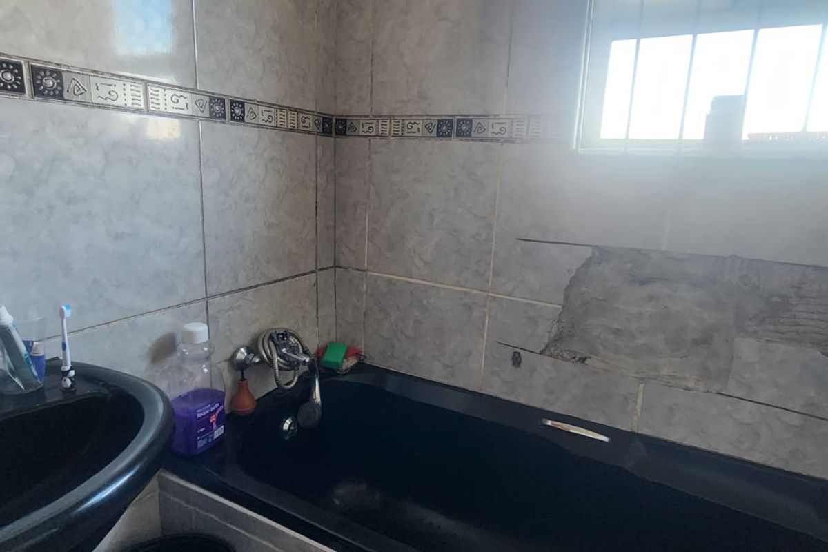 Bathroom featuring a black vanity basin and bathtub, with visible damage to the wall tiling requiring repair and renovation.