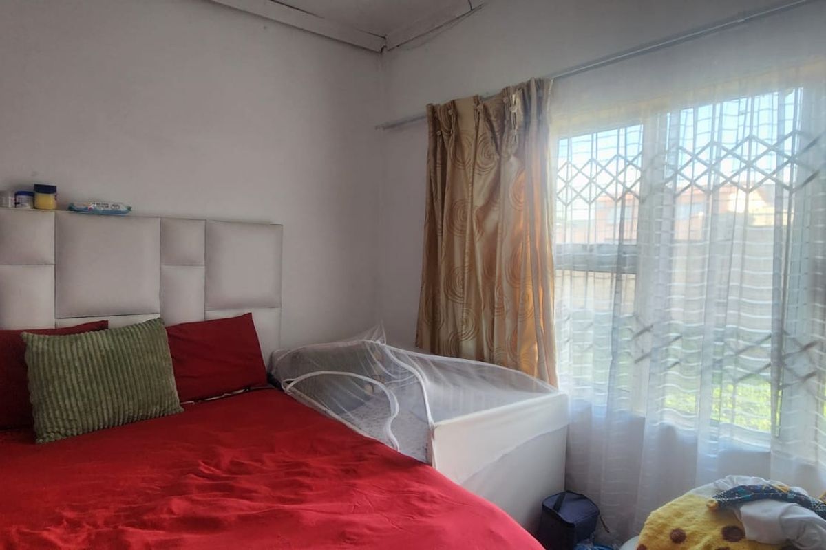 A bedroom featuring a large window with an integrated security gate and curtain rail, providing natural light to the space.