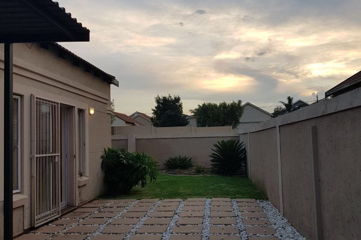A rear exterior view featuring a paved patio area, a small lawn, and high perimeter walls providing privacy.