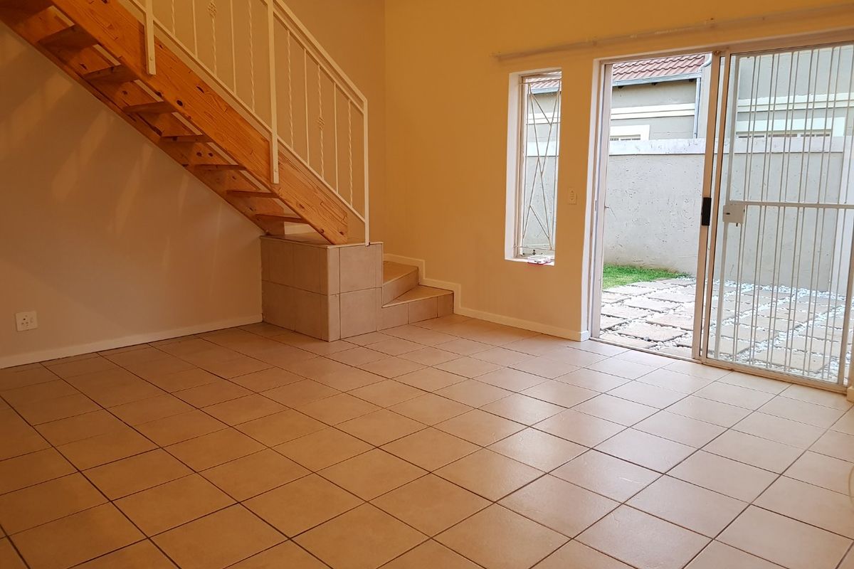 An open-plan living area featuring tiled flooring, a timber staircase with metal balustrade, and direct access to a paved outdoor patio area.