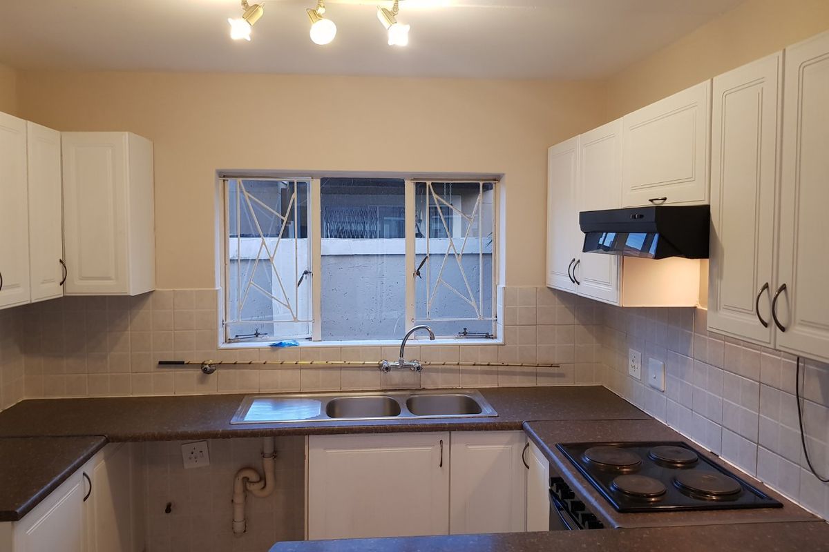 A functional kitchen featuring white cabinetry, a double sink, electric hob with extractor fan, and tiled backsplash, offering a clean and practical workspace.