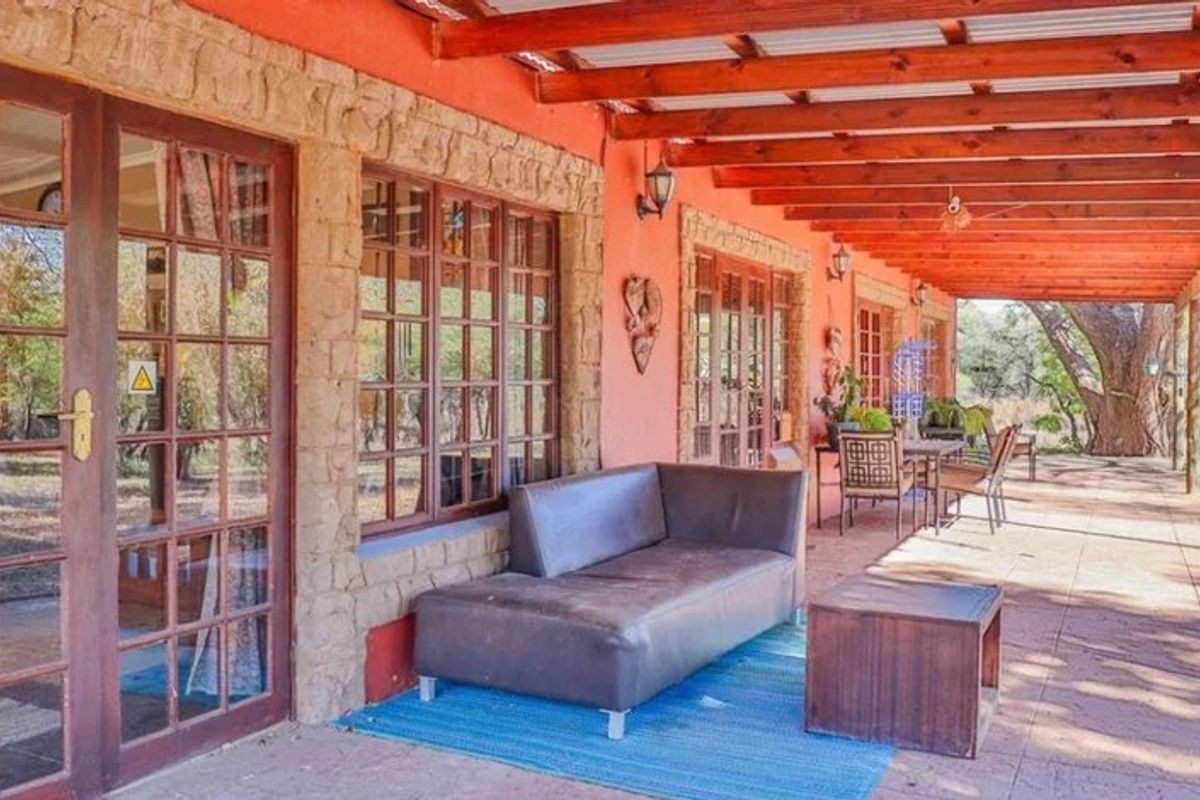 A spacious covered patio featuring a timber pergola, stone-clad exterior walls, and multiple sets of french doors leading into the home.