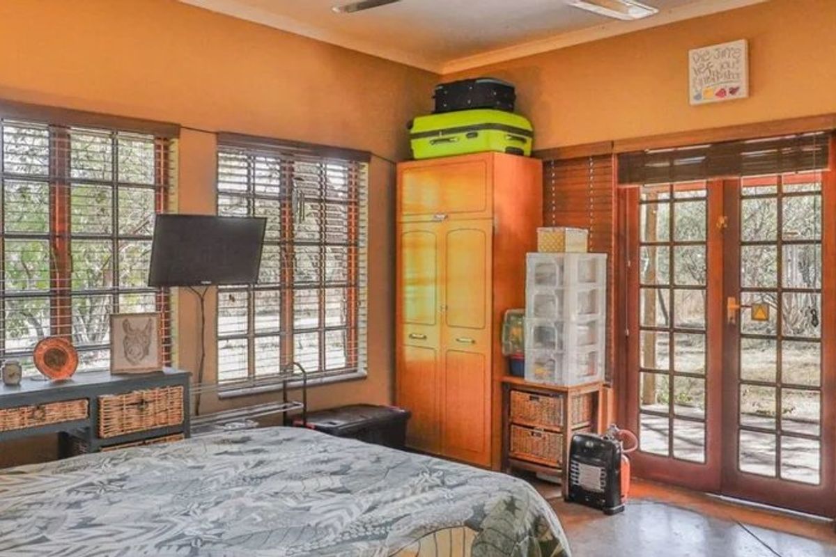A bedroom featuring concrete flooring, timber-framed windows, and french doors providing direct access to the exterior.