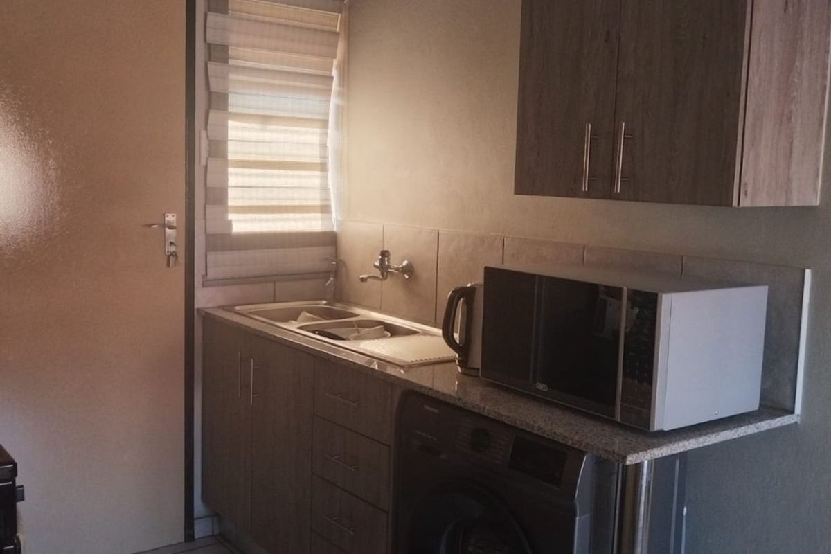 A functional kitchen area featuring built-in cabinetry, a stainless steel sink, tiled backsplash, and tiled flooring with space for a washing machine.