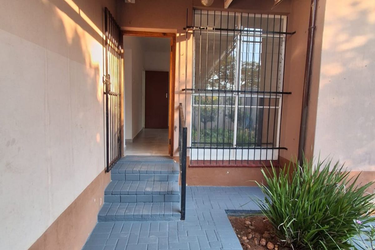 Entrance area featuring a paved walkway, security gate, and covered porch with steps leading into the apartment.
