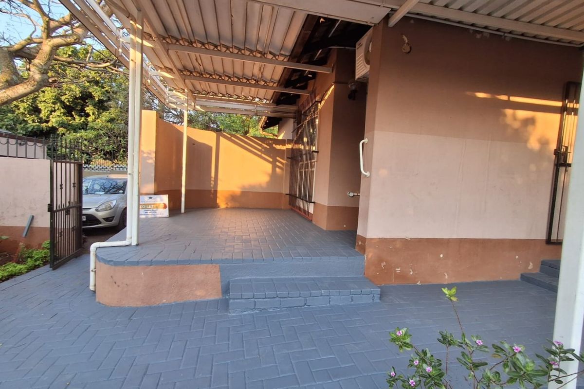 A covered outdoor patio area featuring paved flooring, security gates, and direct access to the building entrance.