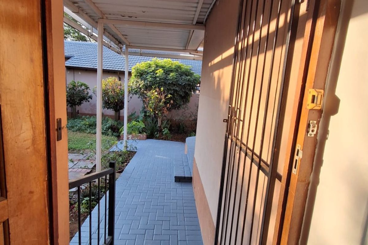 A covered outdoor patio area featuring a paved walkway, security gate, and direct access to the garden space.