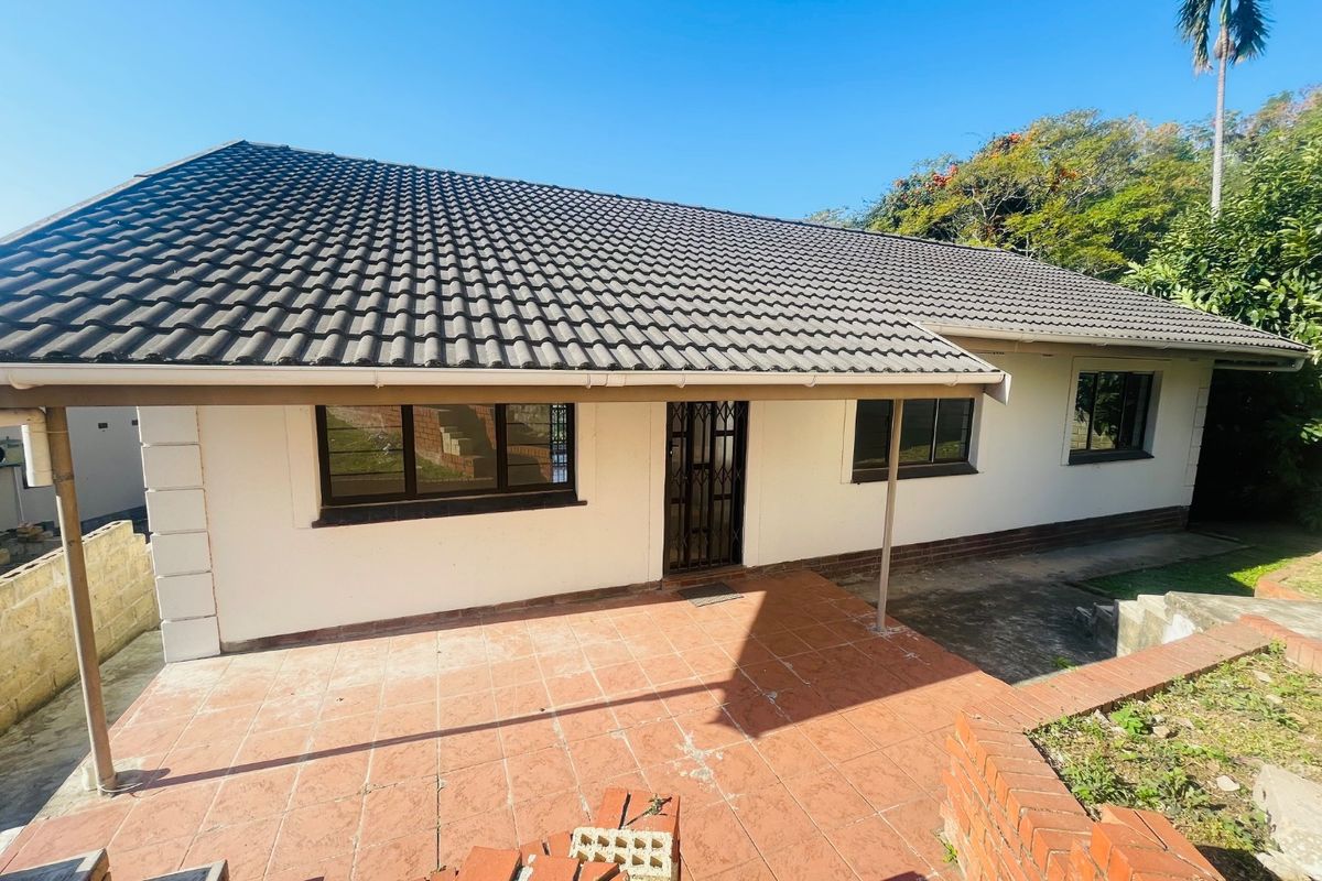 Rear view of the house featuring a covered patio area, tiled roof, and brick retaining wall in a landscaped garden setting.