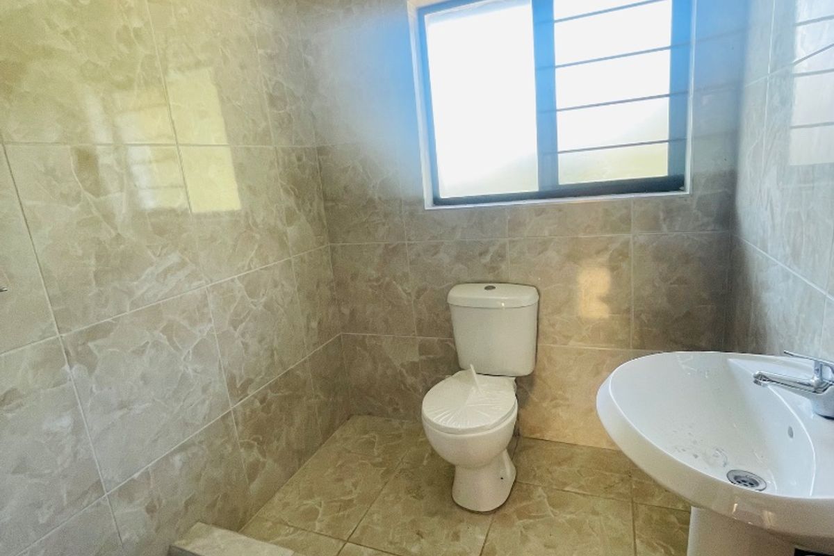A functional bathroom featuring a pedestal basin, toilet, and a tiled shower base with neutral wall and floor tiling.