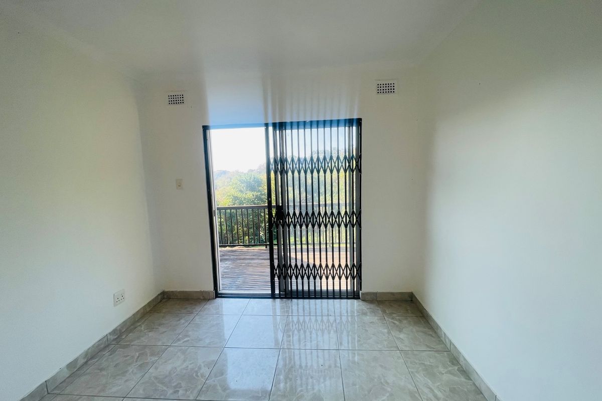 A bright, empty living room featuring neutral tiled flooring and a sliding glass door with a security gate leading to an outdoor balcony.