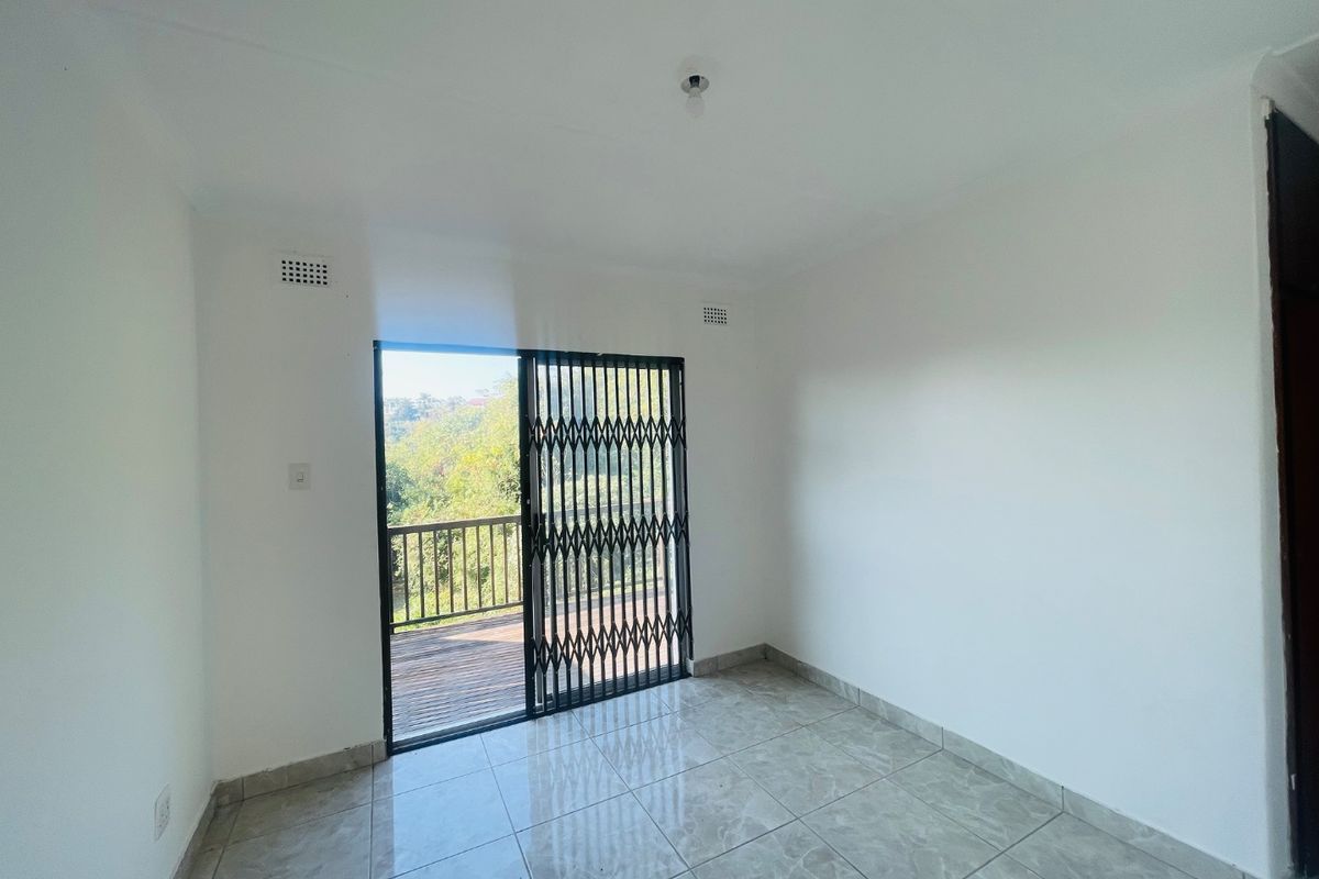 A bright, empty bedroom featuring tiled flooring and a sliding glass door with a security gate leading to an outdoor balcony.