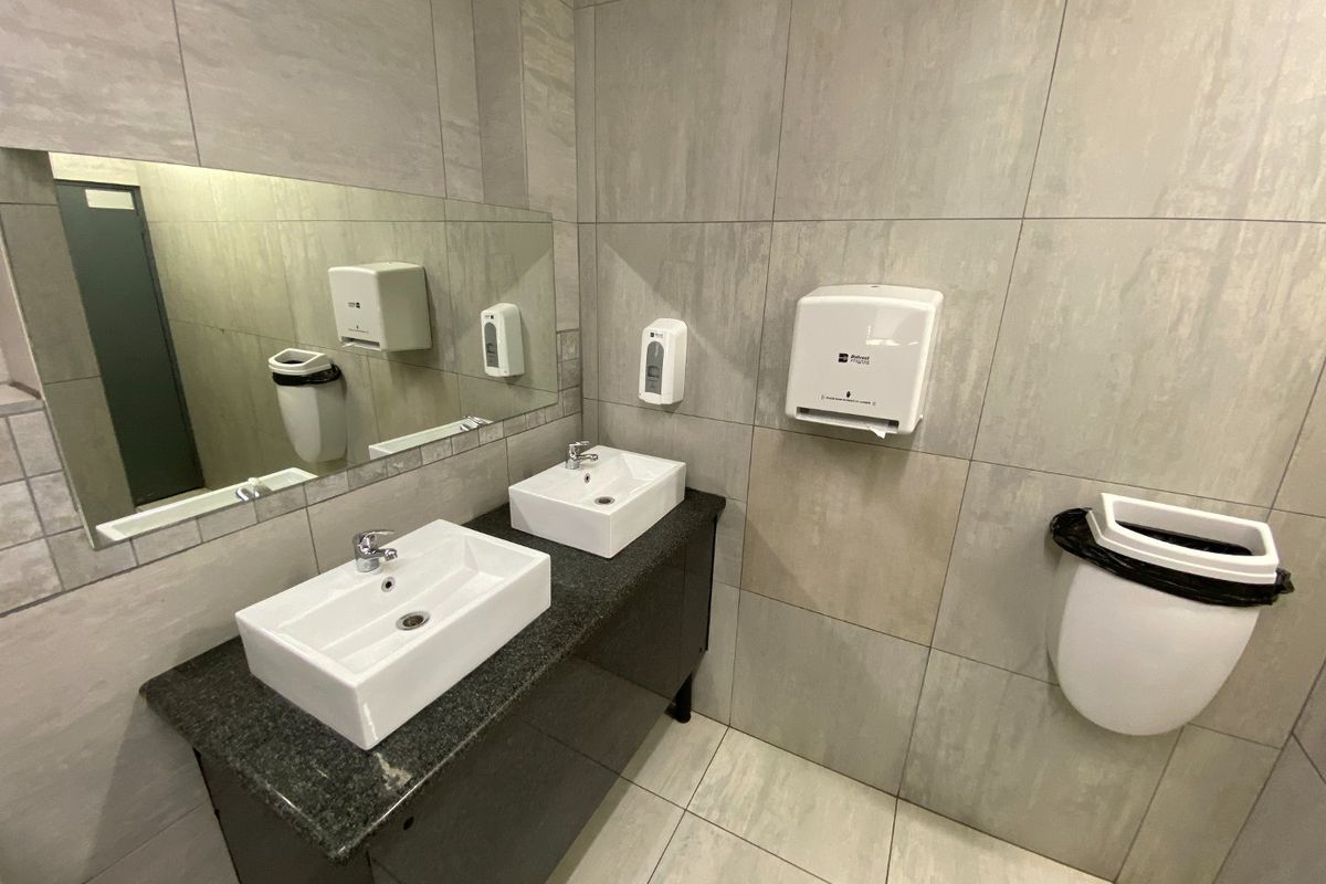 Modern commercial bathroom featuring dual vanity basins with a granite countertop, large wall-mounted mirror, and tiled finishes throughout.