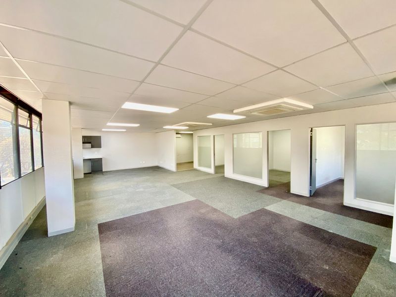Spacious open-plan commercial office space featuring glass partitions, suspended ceilings, recessed lighting, and a small kitchenette area.