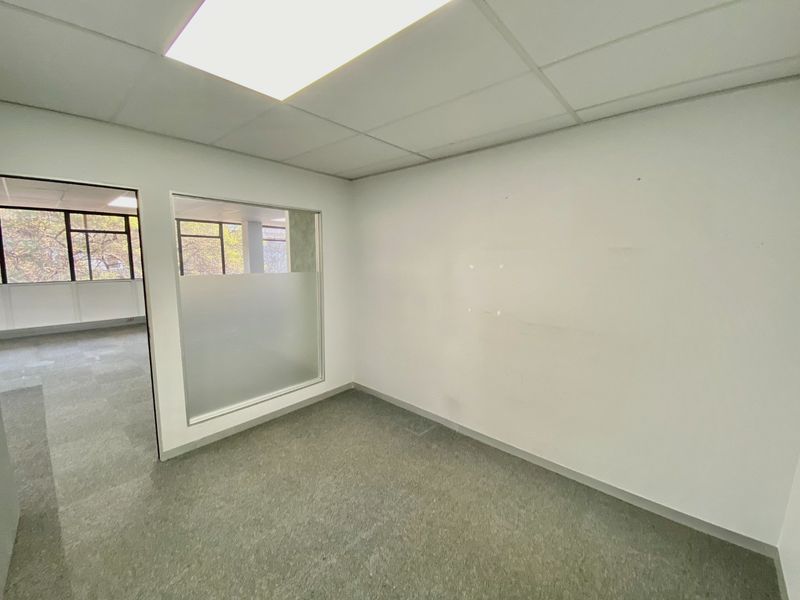 A vacant commercial office space featuring neutral carpet tiles, a suspended ceiling with recessed lighting, and a frosted glass partition wall.