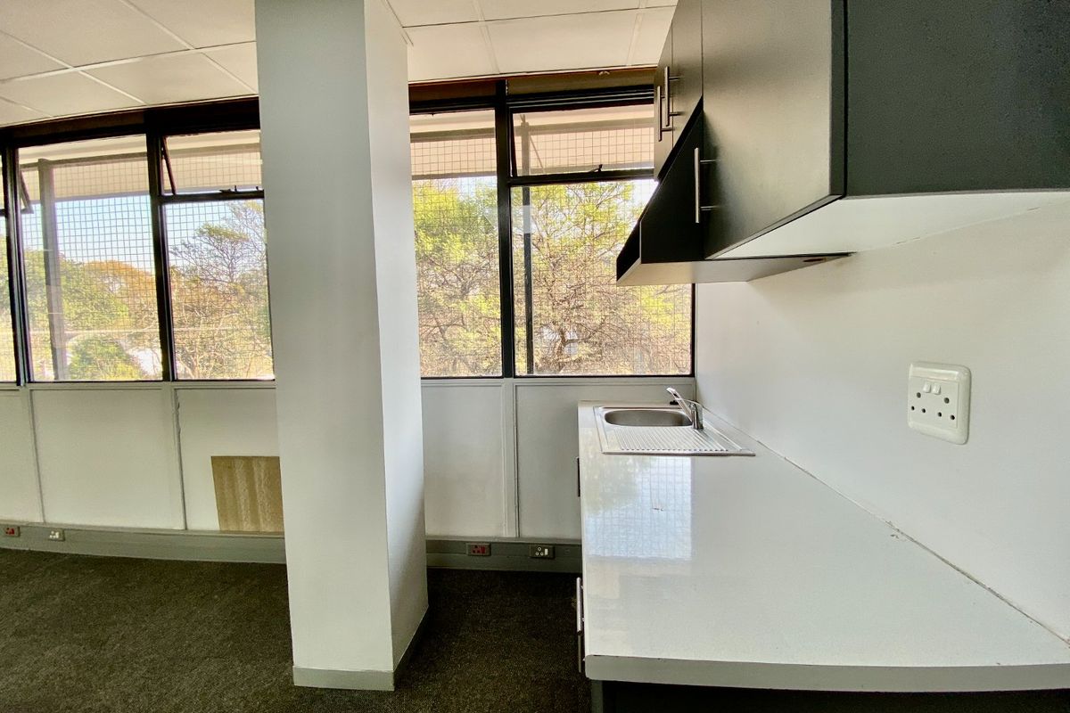 A compact kitchenette area featuring built-in cabinetry, a stainless steel sink, and large windows providing natural light.