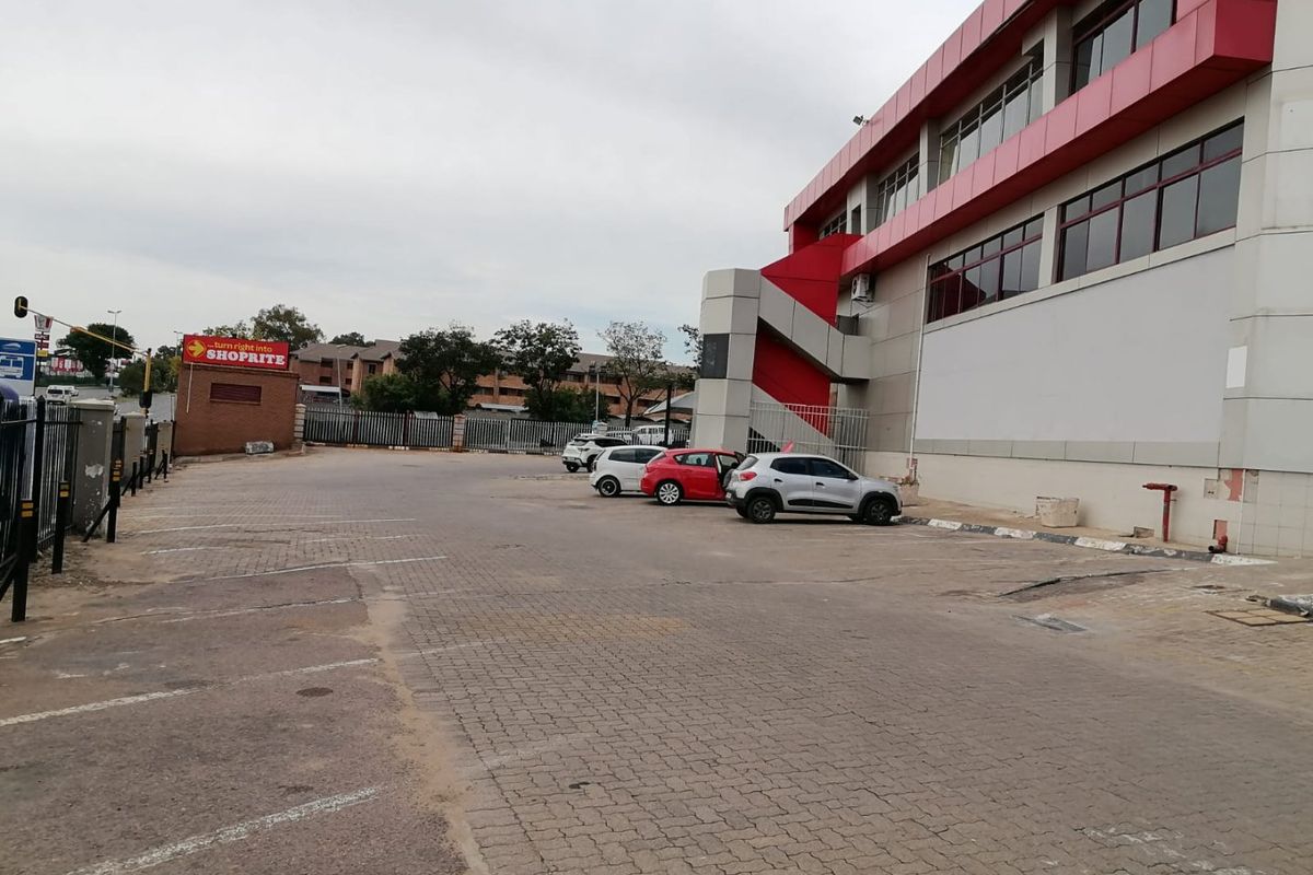 Rear exterior view of a commercial building featuring a paved parking area, external metal staircase, and red-accented facade cladding.