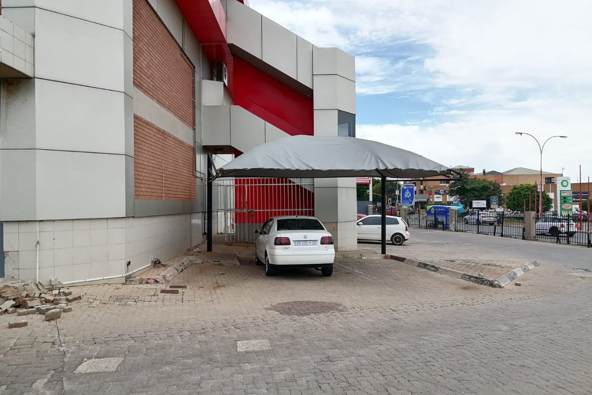 Exterior view of a commercial building featuring a covered parking bay, paved driveway, and metal security gate access.