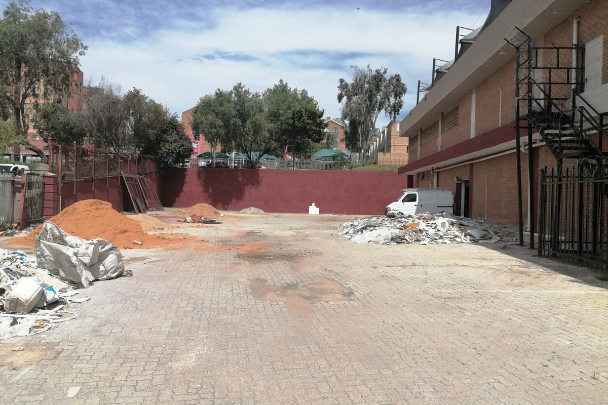 Rear exterior area of the commercial property featuring paved ground, a brick retaining wall, and external metal staircase access, currently requiring site clearance.