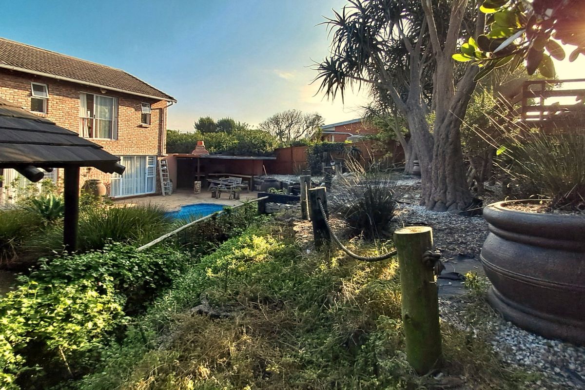 Rear view of a brick house featuring a swimming pool, covered patio area, and established garden with mature trees.