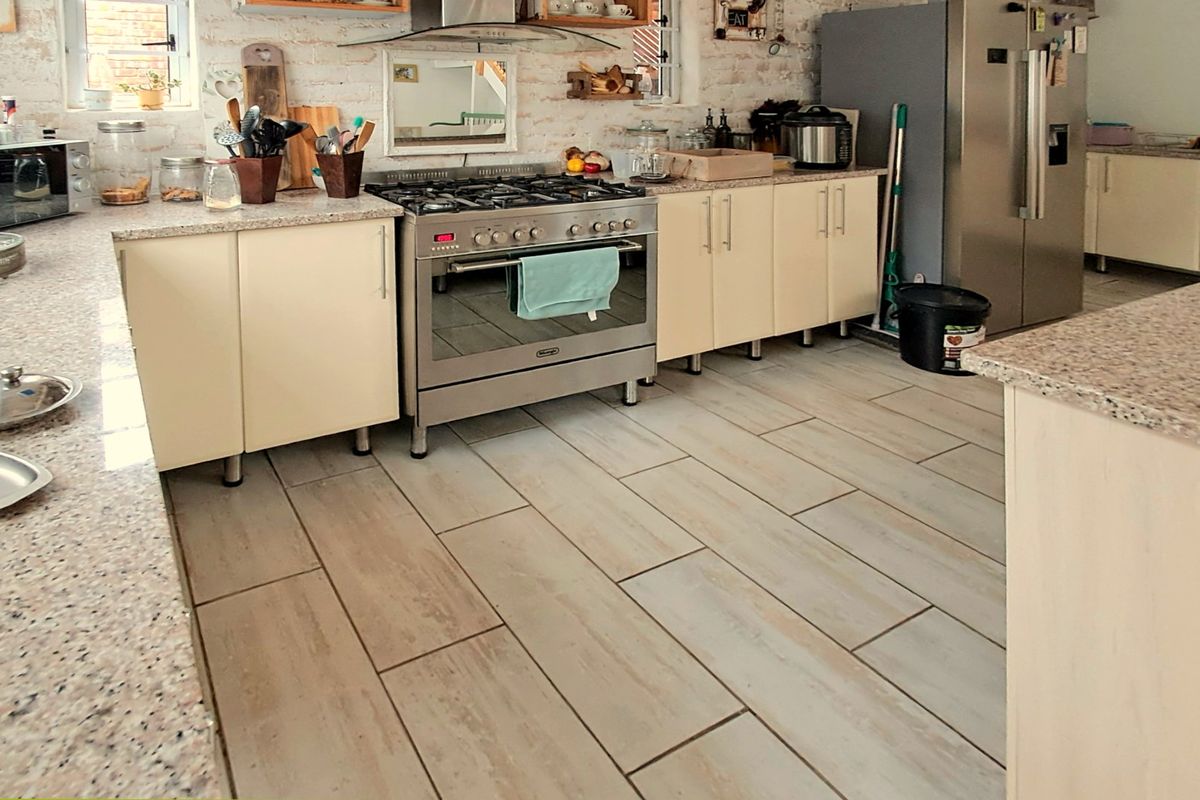 A functional kitchen featuring granite countertops, a gas stove with extractor fan, built-in cabinetry, and light-toned tiled flooring against an exposed brick wall.