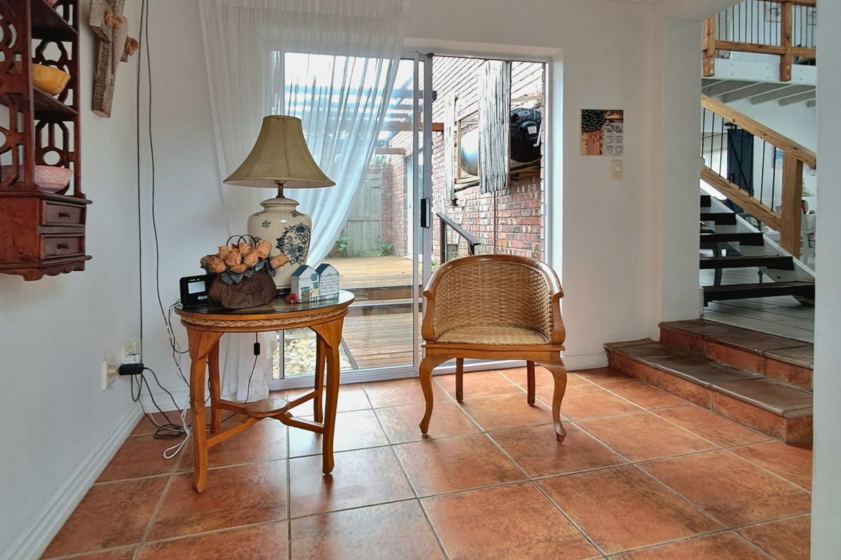 A living area featuring terracotta floor tiles, a sliding glass door leading to an outdoor patio, and an open staircase with wooden treads.