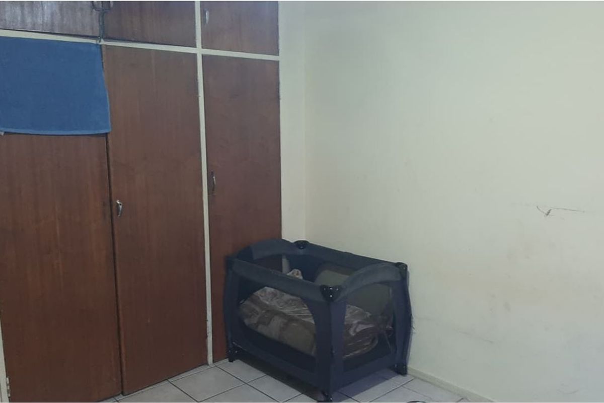 A bedroom featuring built-in wooden cupboards and tiled flooring, requiring cosmetic updates to the wall finishes and cabinetry.