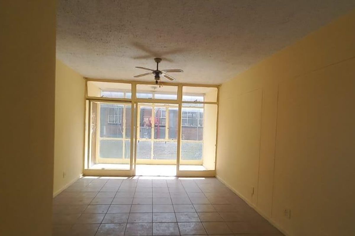An empty living room featuring tiled flooring, a ceiling fan, and large glass doors providing natural light and access to the exterior.
