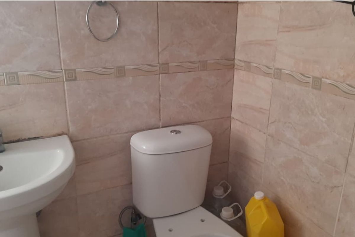 A functional bathroom featuring a pedestal washbasin, a standard toilet, and neutral-toned ceramic wall tiling.