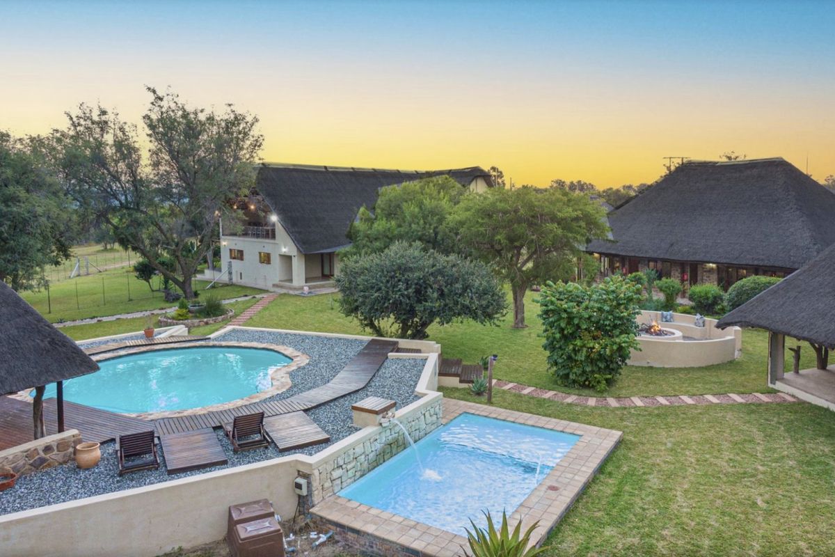Aerial view of a farm property featuring multiple thatched-roof buildings, a swimming pool, a plunge pool, and a landscaped garden with a fire pit.