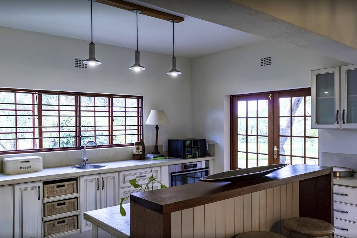 A well-maintained kitchen featuring classic cabinetry, stone countertops, built-in oven, and pendant lighting, with direct access to the garden through timber-framed french doors.
