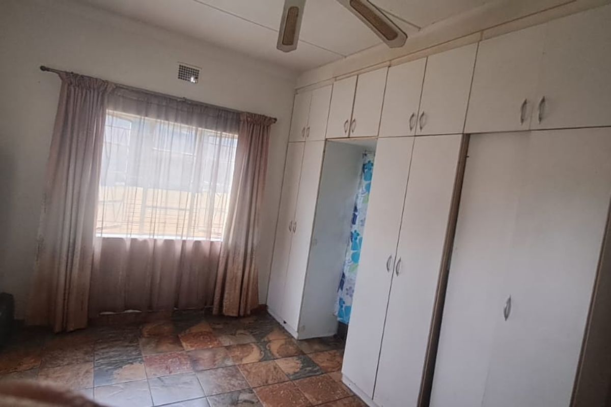 A bedroom featuring built-in cupboards, a ceiling fan, and tiled flooring. The space is dated and would benefit from cosmetic updates.