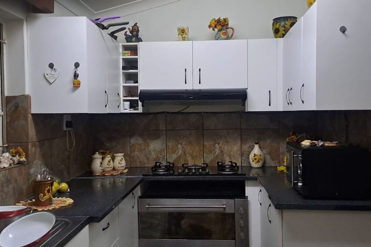 A functional kitchen featuring white cabinetry, dark countertops, a gas hob with extractor fan, and stone-look wall tiling.