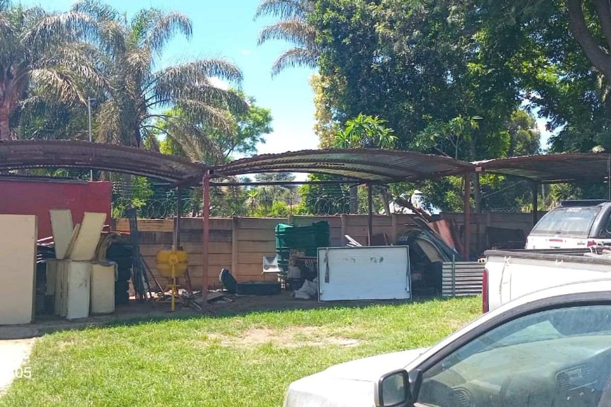 Rear yard area featuring a large, weathered corrugated metal carport structure and perimeter fencing with razor wire.