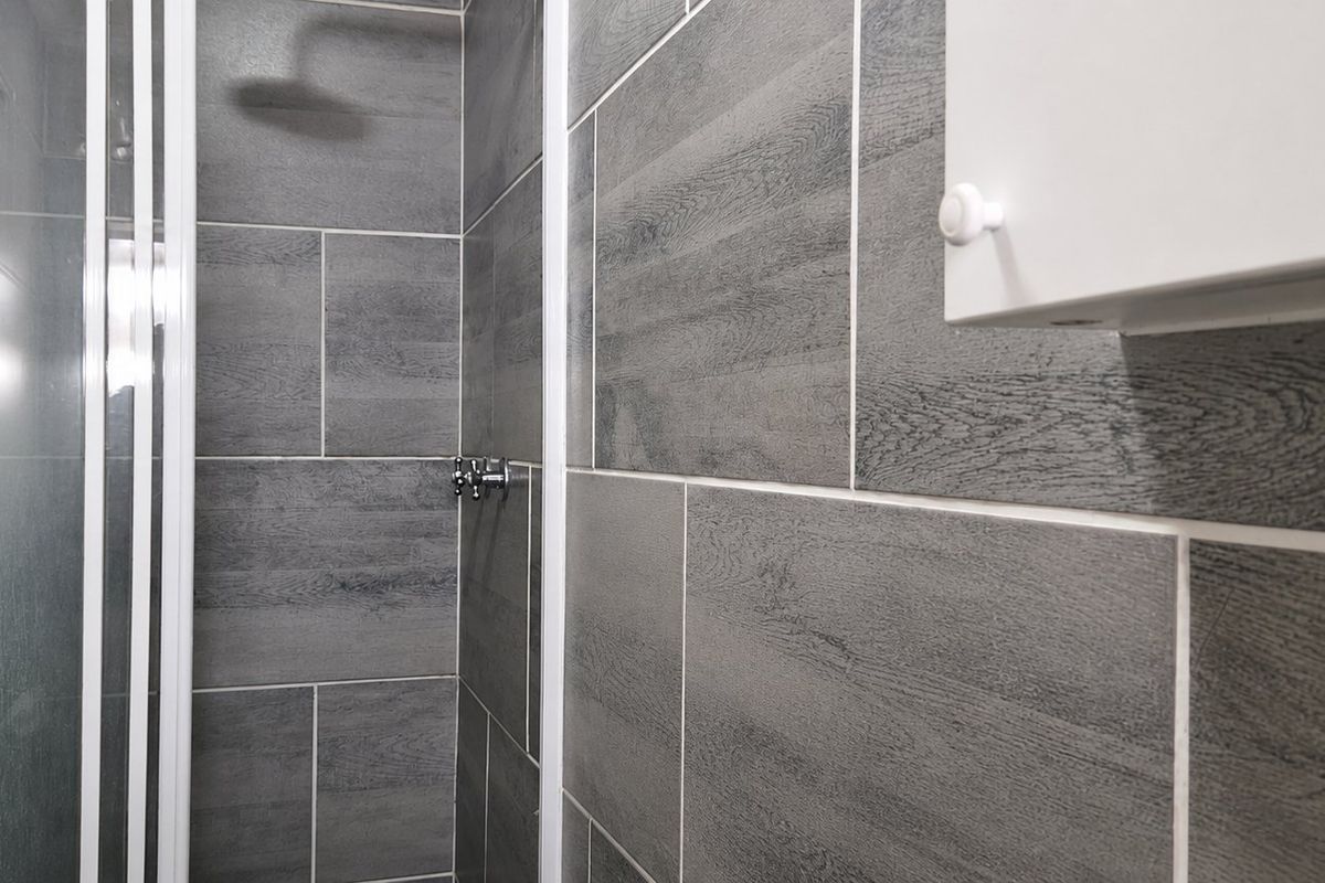 A modern bathroom shower area featuring grey wood-look wall tiles, a glass shower enclosure, and a wall-mounted storage cabinet.