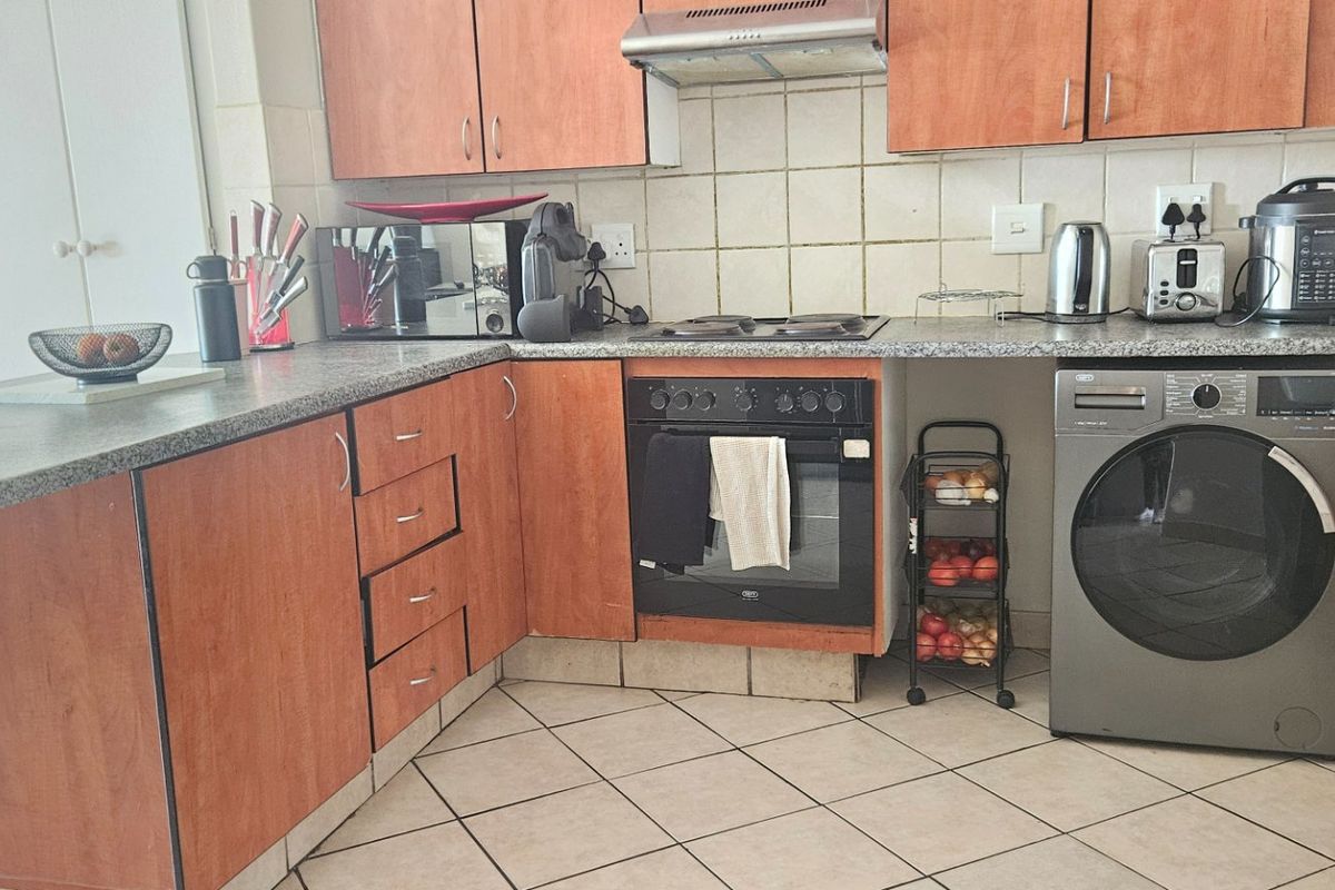 Functional kitchen featuring laminate cabinetry, granite-look countertops, ceramic tile backsplash, built-in oven, electric hob, extractor fan, and integrated laundry plumbing.