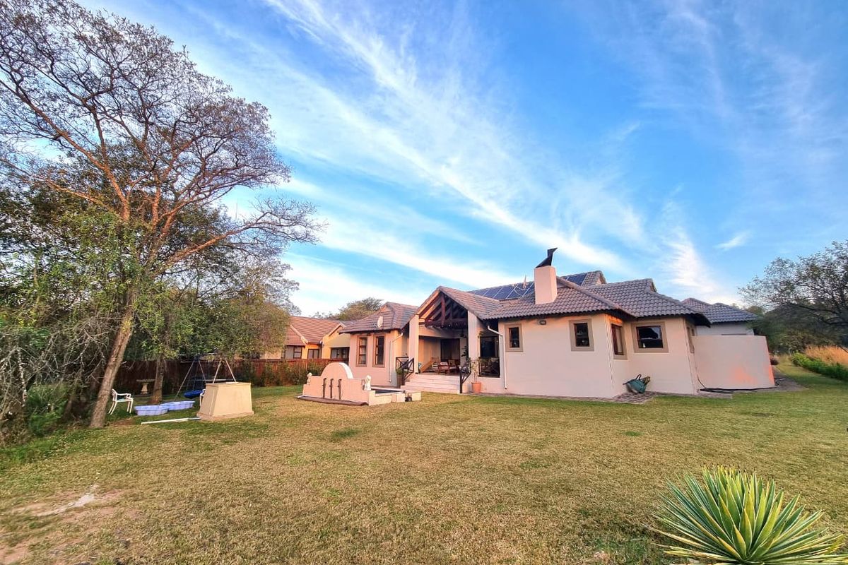 Rear view of the property featuring a spacious garden, covered patio with timber trusses, tiled roof, and installed solar panels.