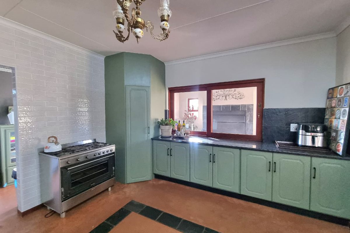 A functional kitchen featuring sage green cabinetry, granite countertops, a gas stove with oven, and a decorative chandelier.