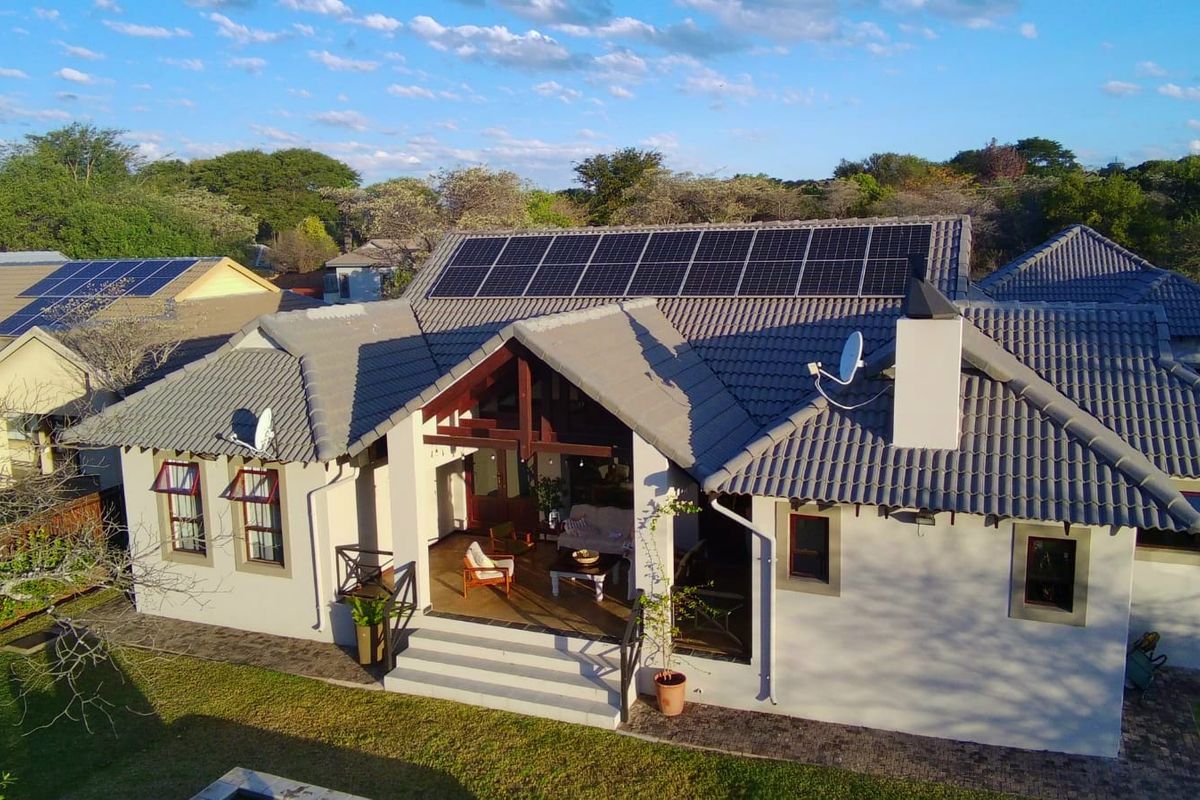 Aerial view of a residential property featuring a tiled roof with integrated solar panels, a chimney, and a covered rear patio area.