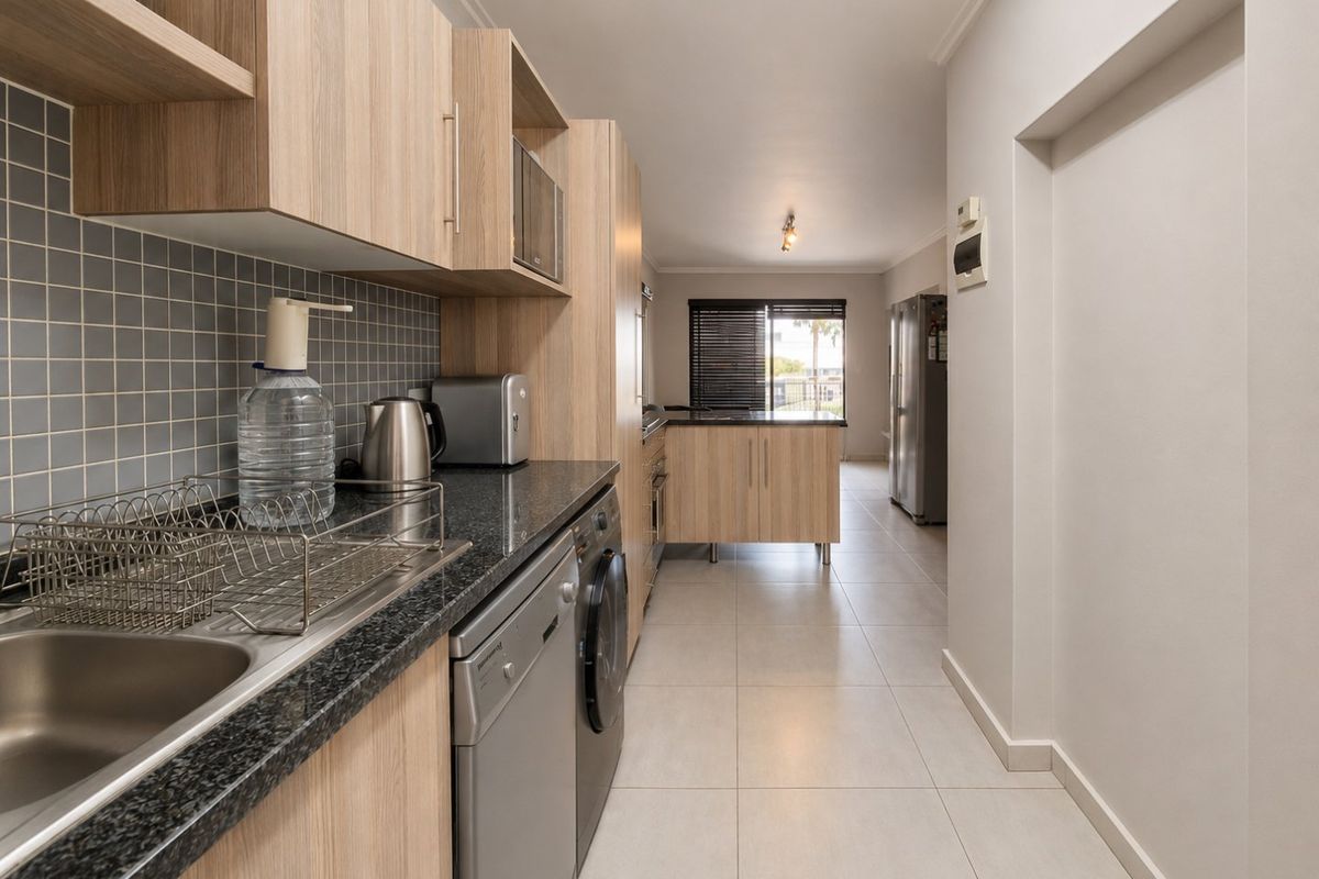 Modern kitchen featuring light wood cabinetry, granite countertops, tiled backsplash, and integrated appliances, leading into an open-plan living area.
