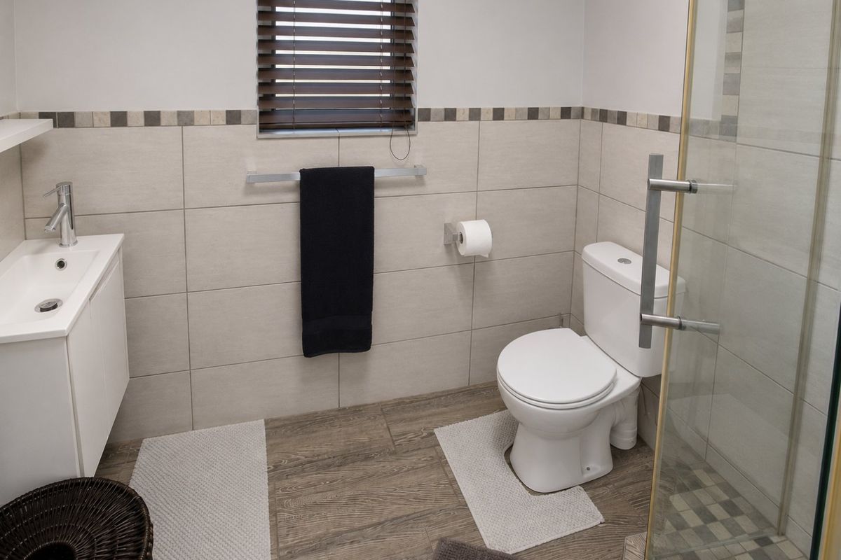 A modern bathroom featuring a vanity with basin, a toilet, and a glass-enclosed shower with neutral wall tiles and wood-look flooring.