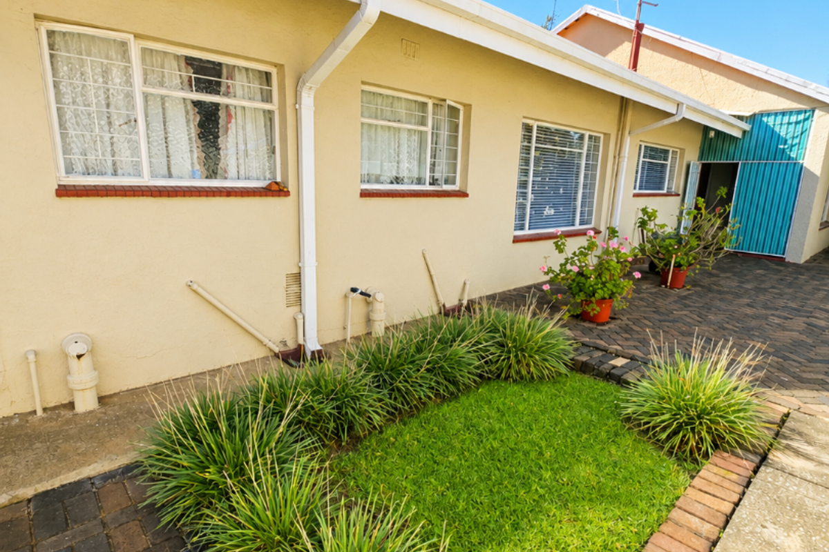 Rear exterior view of the house featuring a paved courtyard, small garden patch, and functional exterior infrastructure including guttering and security window bars.