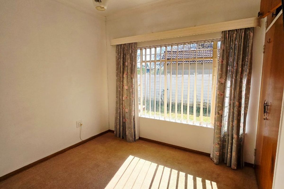 A vacant bedroom featuring built-in wardrobe storage, carpeted flooring, and security bars on the window.